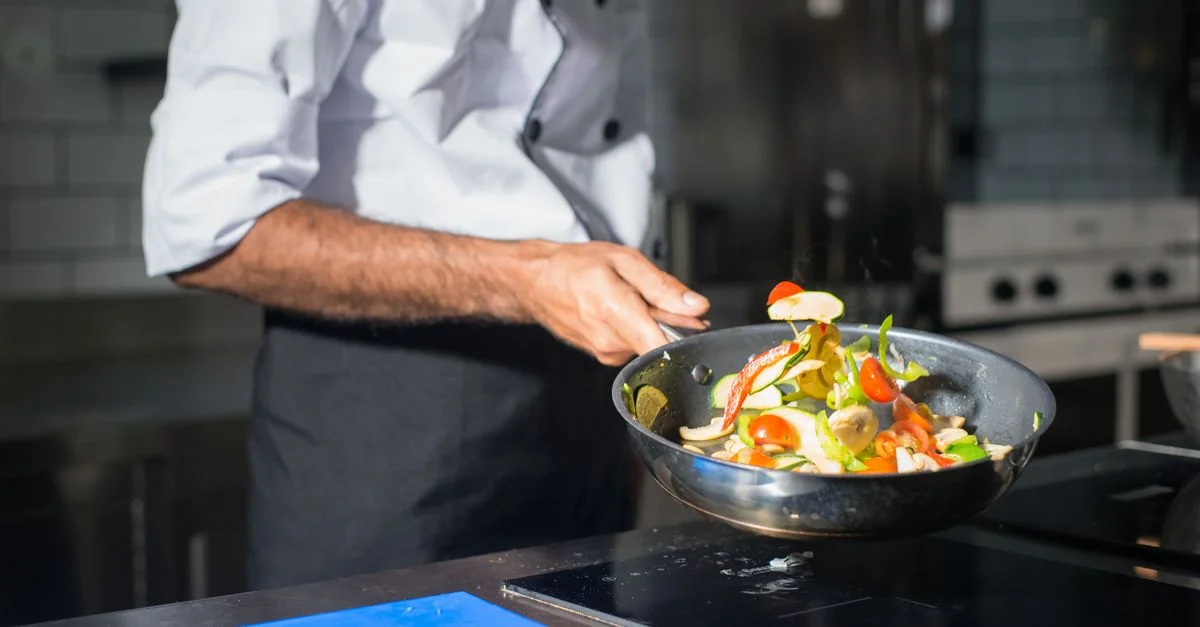 Chef professionnel faisant sauter des légumes frais dans une poêle dans une cuisine moderne.