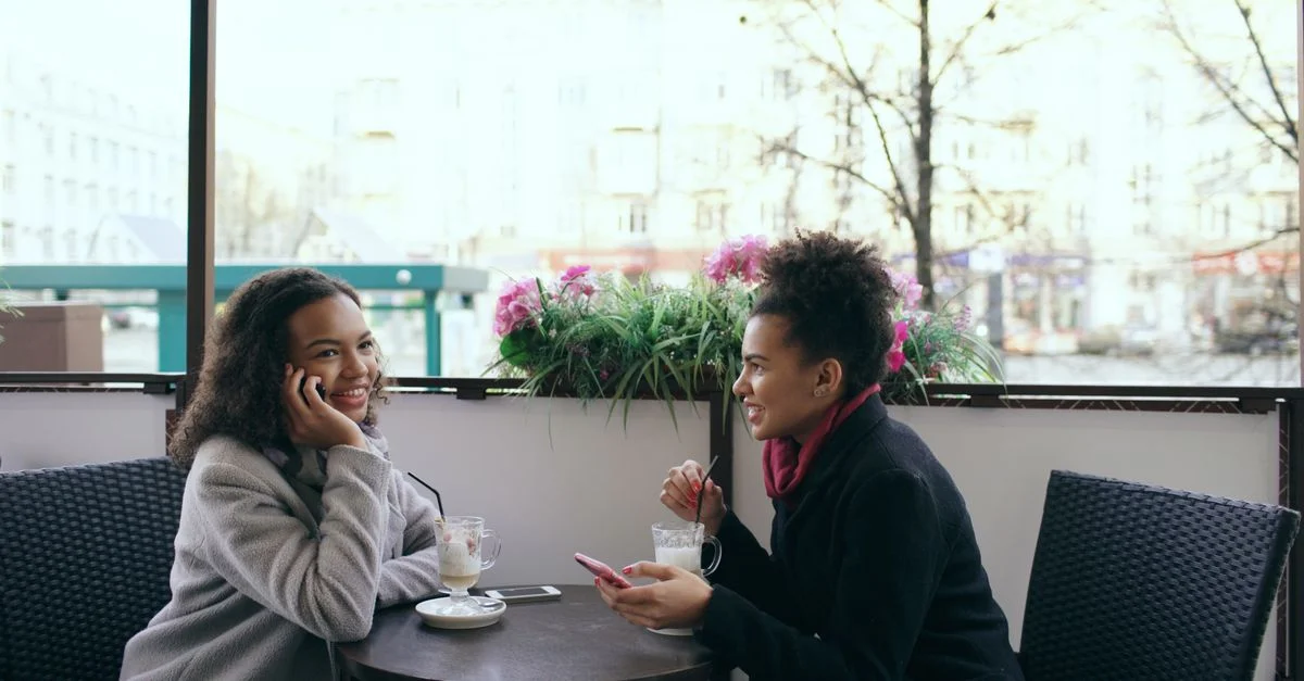 Deux femmes savourant un café et discutant dans un cadre de café extérieur.