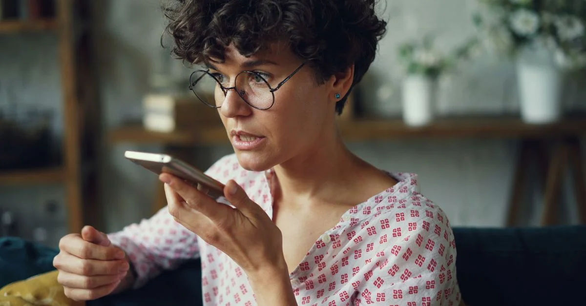 Femme décontractée utilisant la commande vocale sur un smartphone à la maison.