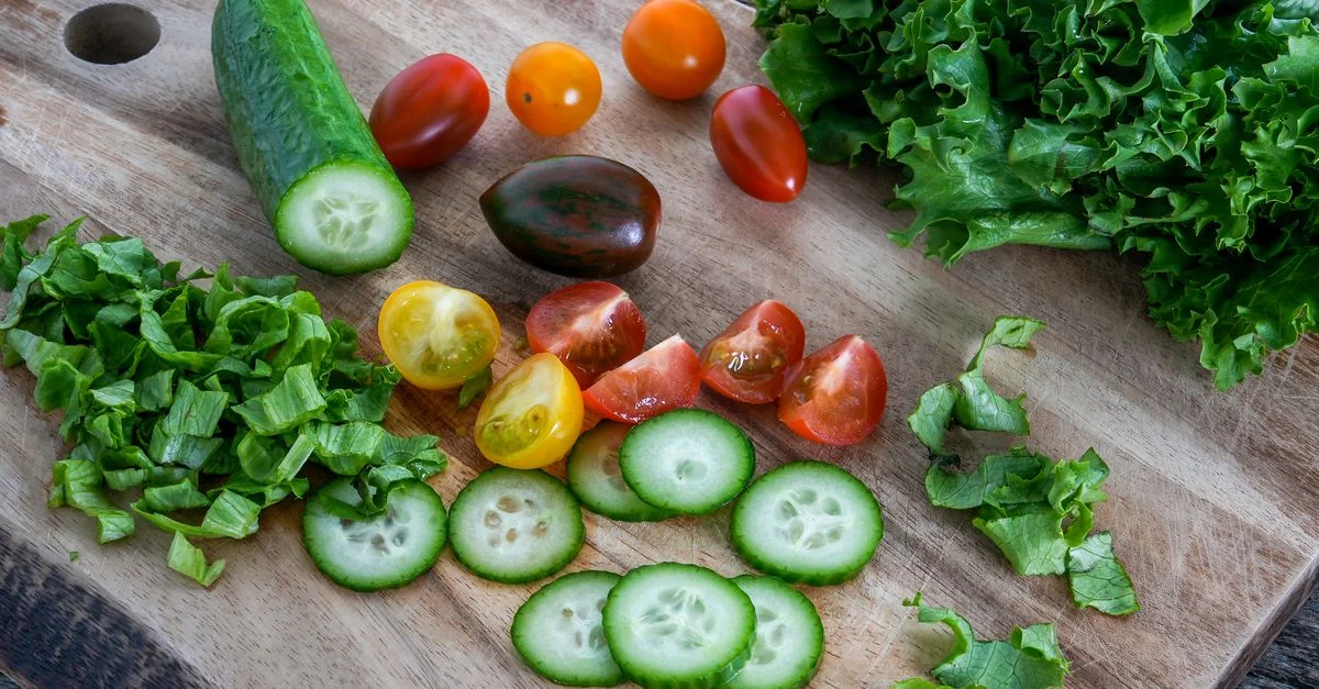 Un mélange vibrant de concombres tranchés, de tomates cerises et de laitue sur une planche à découper en bois, parfait pour les salades.