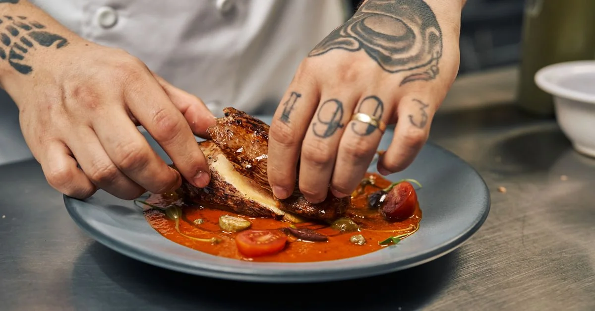 Gros plan sur un chef dressant une assiette avec un plat gastronomique composé de poulet et de tomates.