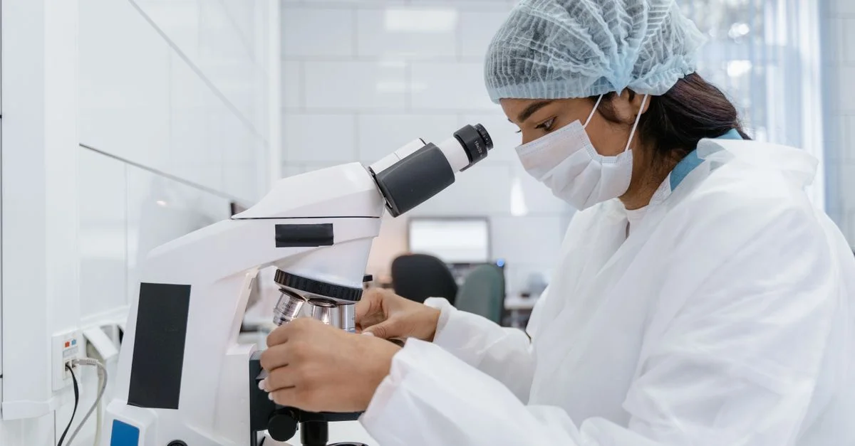 Une scientifique portant un équipement de protection analyse des échantillons à l'aide d'un microscope dans un laboratoire moderne.