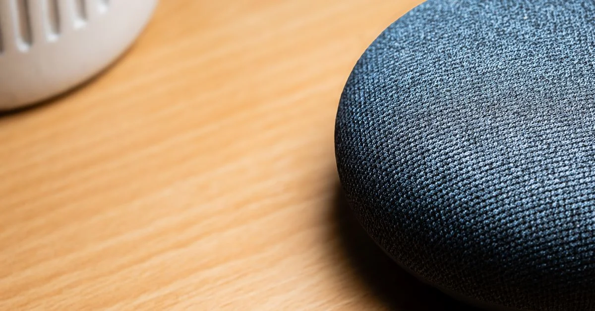 Gros plan d'une enceinte connectée posée sur une table en bois, révélant les détails de sa texture.