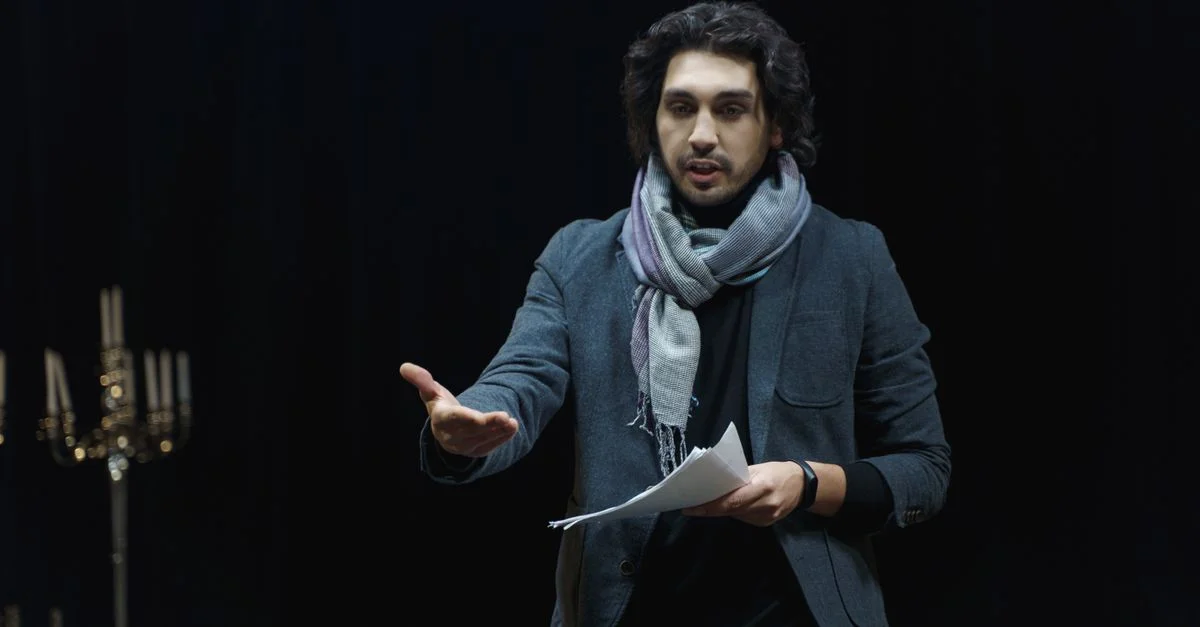 Acteur répétant sur une scène de théâtre sombre, tenant un script et gesticulant de manière dynamique.