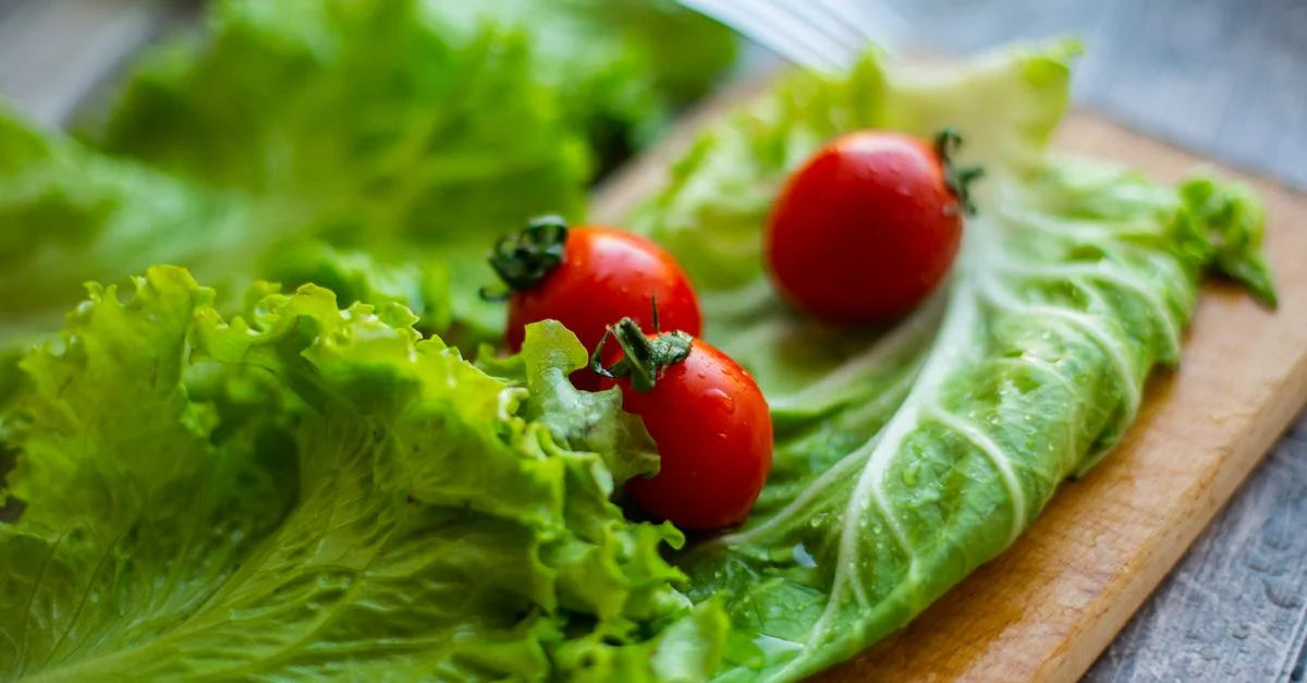 Une laitue verte vibrante et des tomates mûres disposées sur une planche à découper en bois, idéales pour des concepts de repas sains.