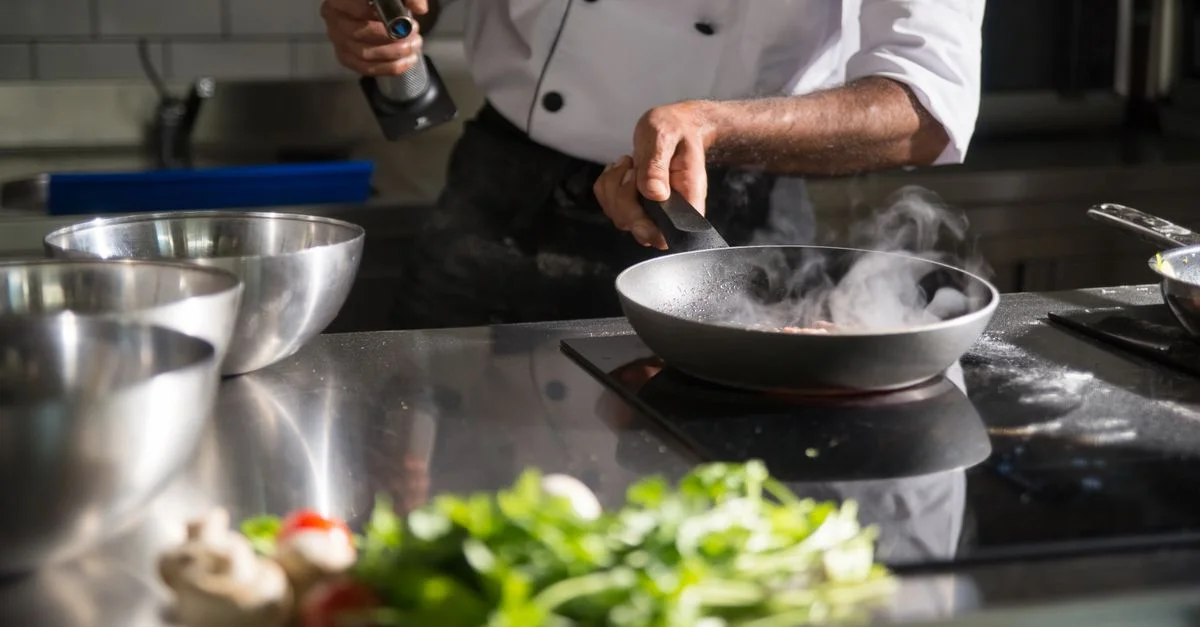 Un chef prépare de la nourriture dans une cuisine élégante en utilisant une poêle sur une plaque de cuisson à induction.