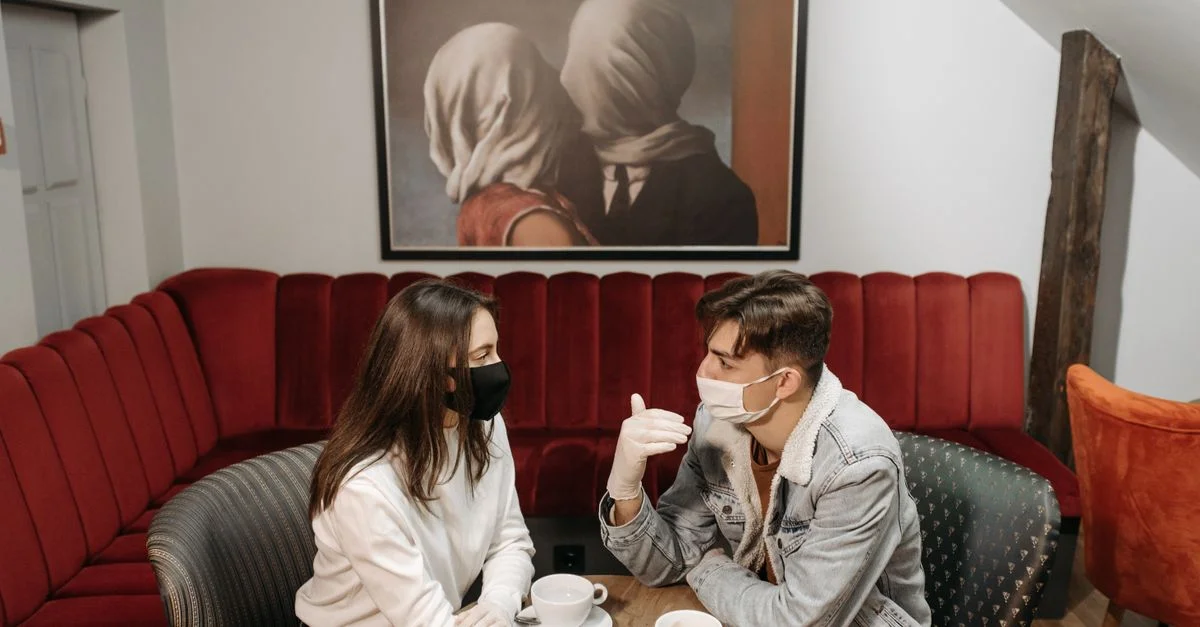 Un couple déguste un café tout en portant des masques dans un café confortable, mettant en avant l'impact de la pandémie.