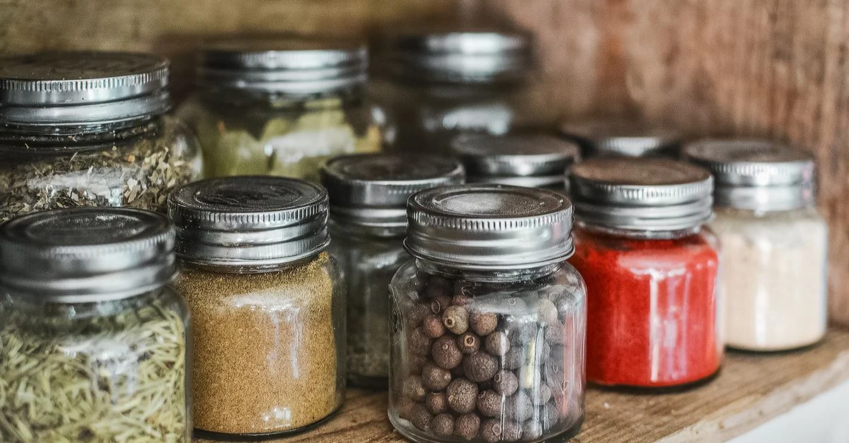 Gros plan sur des bocaux d'épices variés avec différentes herbes sur une étagère de cuisine, mettant en valeur des ingrédients culinaires colorés.