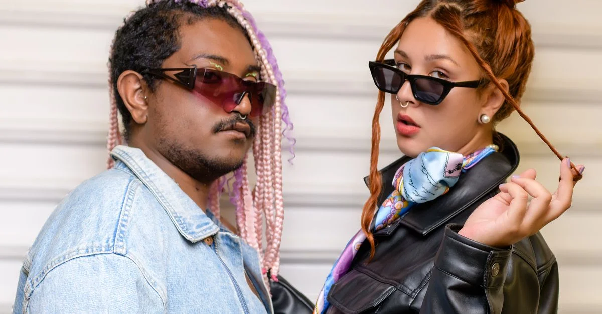 Un couple à la mode portant des lunettes de soleil et une tenue élégante pose avec confiance, mettant en valeur les tendances modernes.