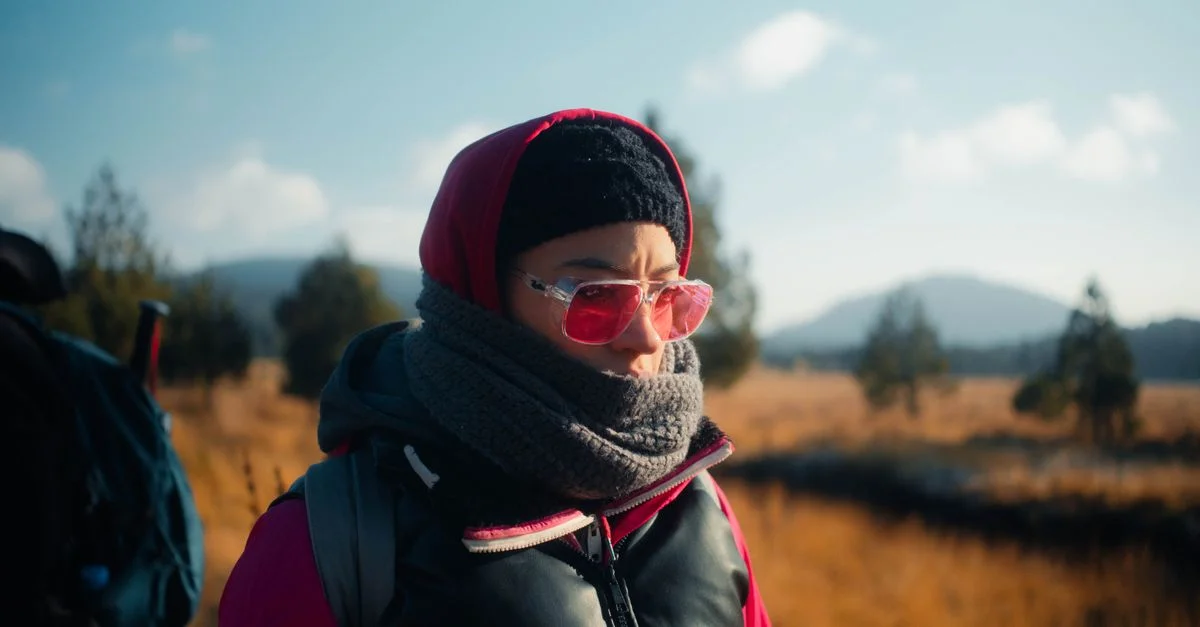 Une personne chaudement vêtue, portant des lunettes de soleil roses, profitant d'une randonnée automnale.