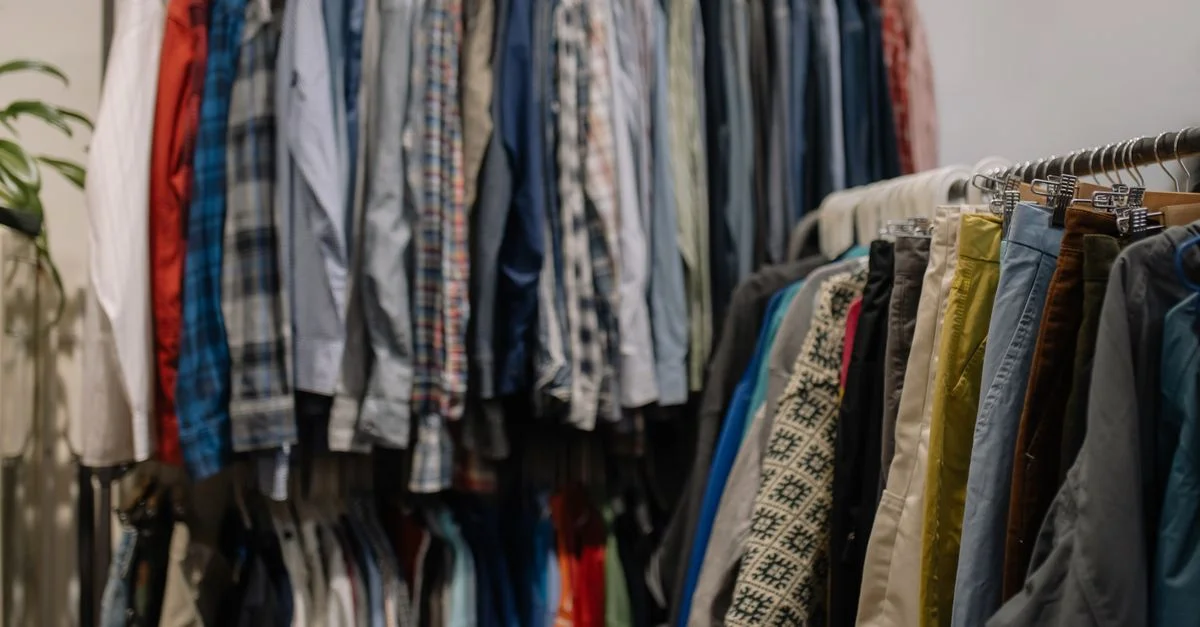 Vêtements variés sur des portants dans un magasin de seconde main, présentant divers styles et couleurs.