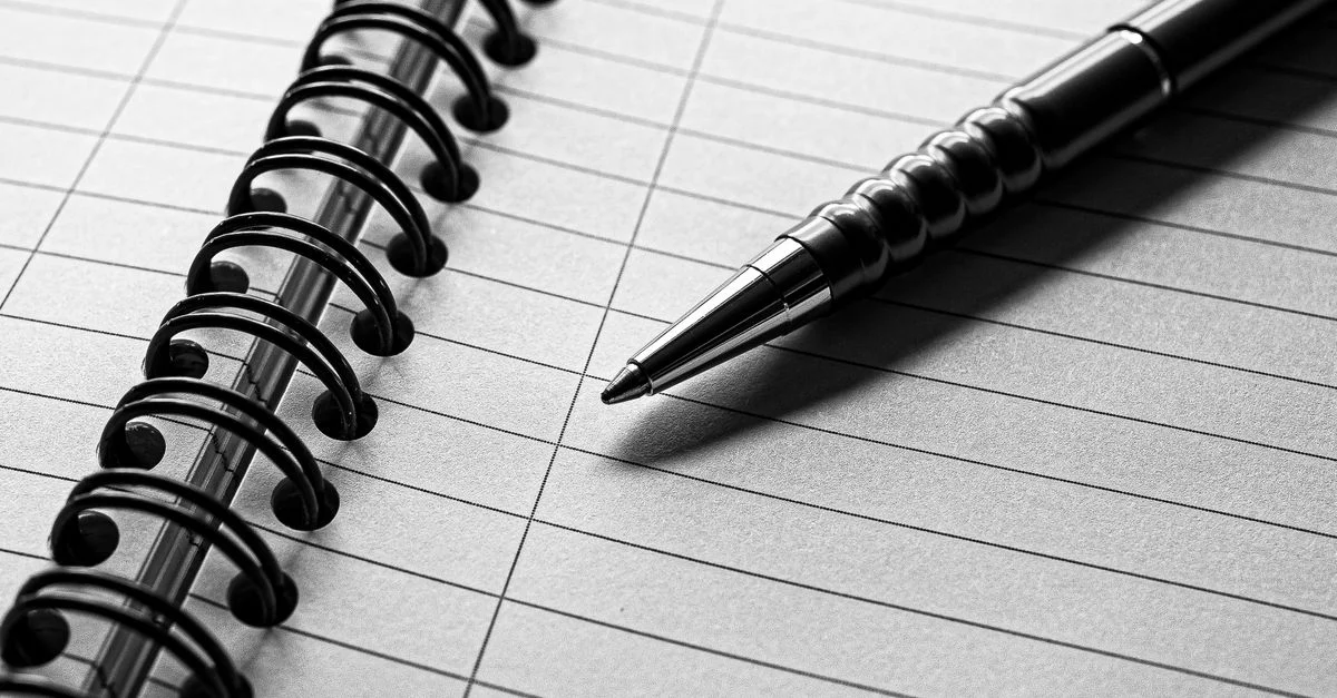 Un élégant stylo en métal repose sur un cahier à spirale aux pages lignées aux tons monochromes.