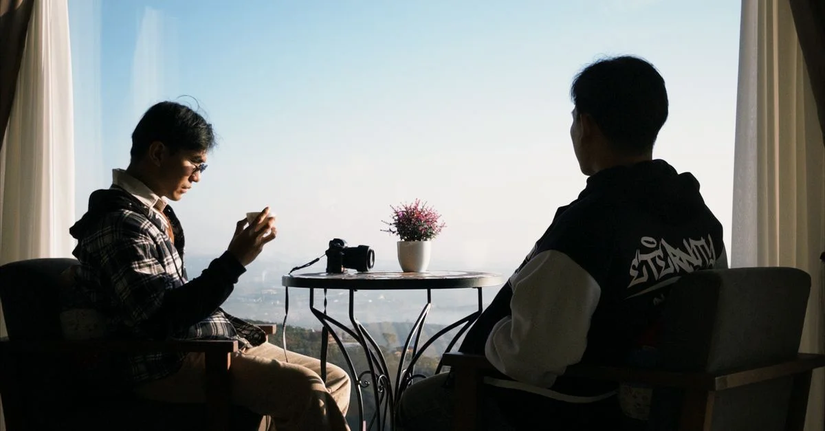 Deux hommes sont assis près d'une fenêtre avec un appareil photo, profitant d'une vue pittoresque en plein jour.
