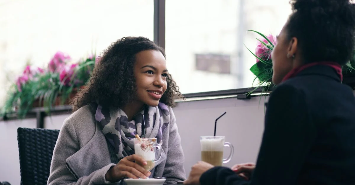 Deux femmes discutant autour d'un café dans un café douillet avec des fleurs en arrière-plan.