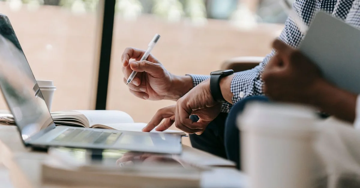 Gros plan sur des collègues discutant de travail en utilisant un ordinateur portable et un carnet dans un bureau intérieur.