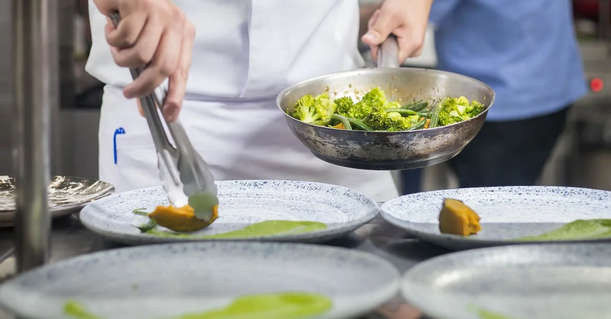 Chef dressant un plat avec des brocolis et des légumes dans un cadre de cuisine professionnel.