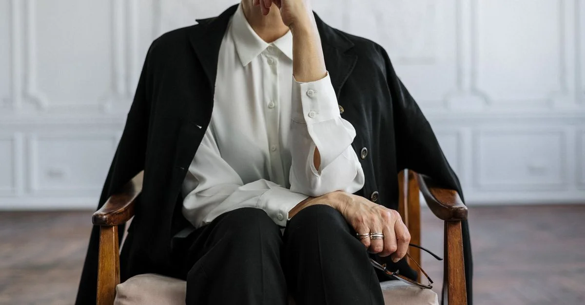 Femme confiante assise en pensée, symbolisant la force et l'intelligence dans un bureau moderne.