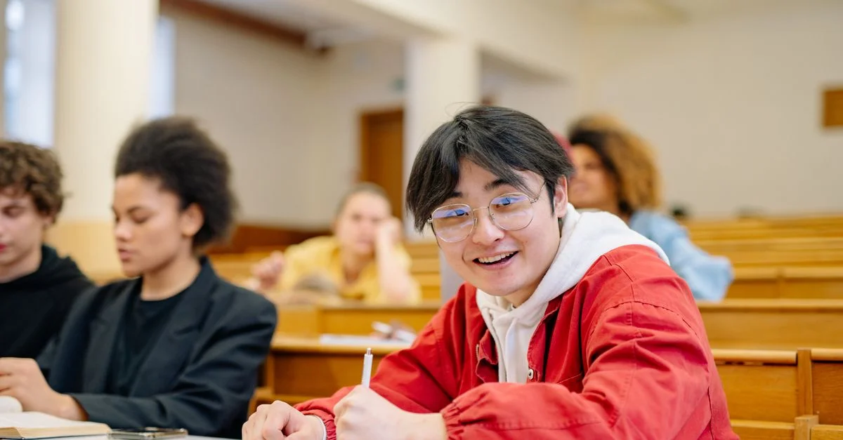 Un étudiant joyeux portant des lunettes est assis dans une salle de conférence universitaire et prend des notes pendant un cours.