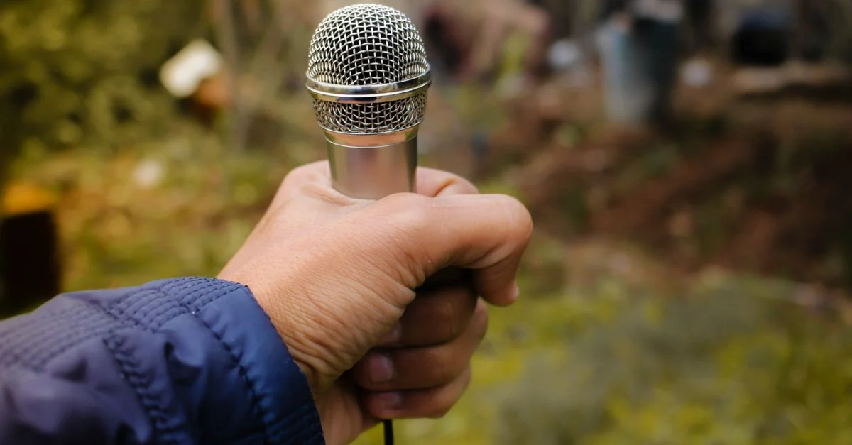 Un gros plan d'une main tenant un microphone argenté dans un environnement extérieur, capturant la mise au point et le détail.
